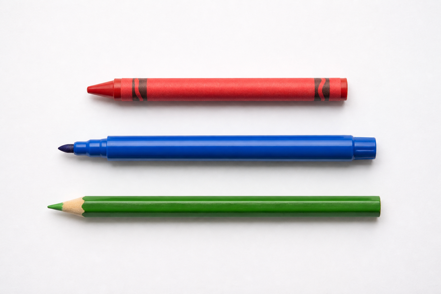 A single red crayon, a blue felt-tip marker, and a green colored pencil lying in a neat row on a clean sheet of white paper, top-down flat lay photo, soft natural light, bright cheerful colors, no tex
